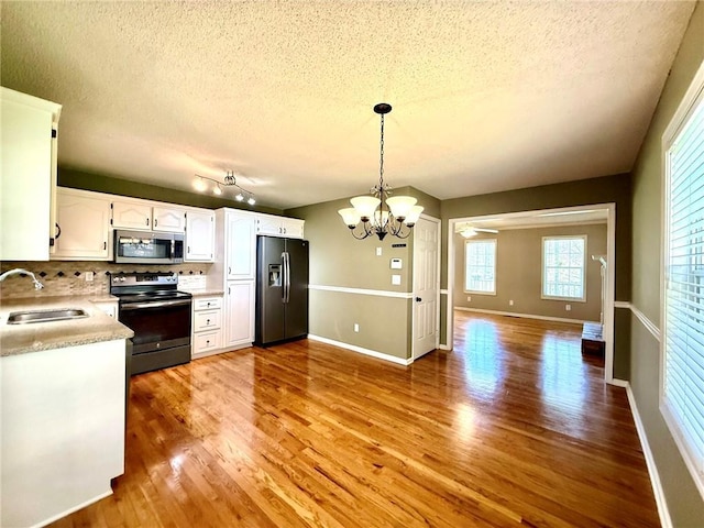 kitchen featuring a sink, electric range oven, light wood-style floors, stainless steel microwave, and black fridge