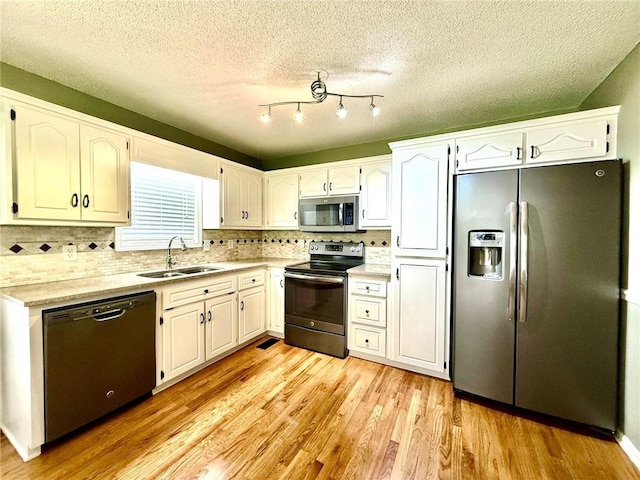 kitchen featuring tasteful backsplash, light wood-type flooring, stainless steel appliances, white cabinetry, and a sink