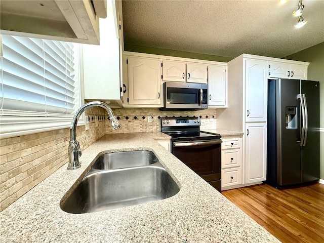 kitchen with a sink, stainless steel appliances, wood finished floors, and white cabinetry