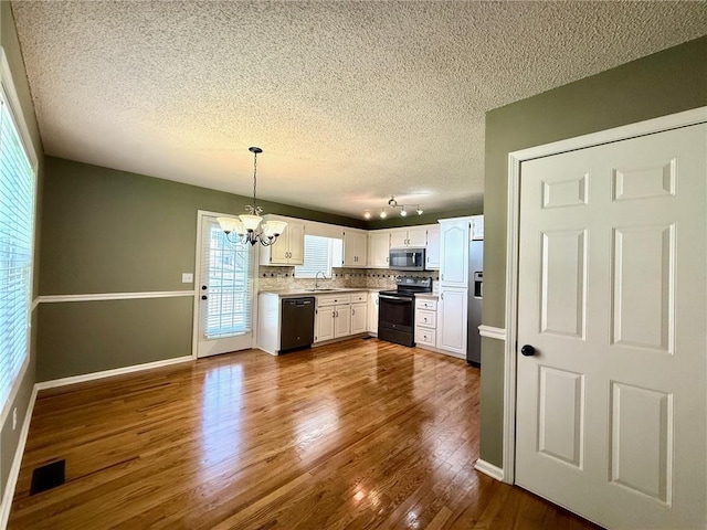 kitchen with dark wood-style floors, visible vents, a sink, black appliances, and a notable chandelier