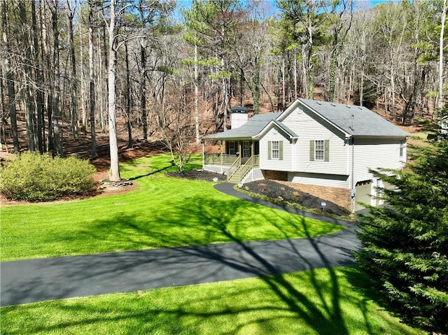 view of front facade with driveway, a chimney, a wooded view, and a front lawn