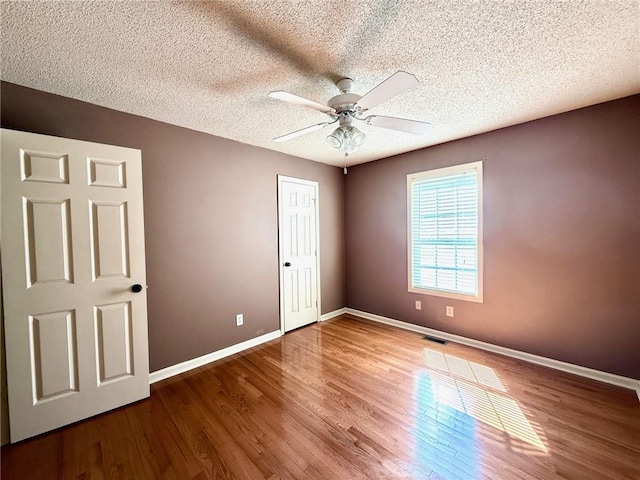 unfurnished bedroom featuring visible vents, a textured ceiling, baseboards, and wood finished floors