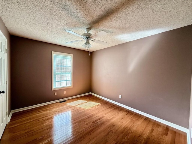 empty room with visible vents, a textured ceiling, wood finished floors, baseboards, and ceiling fan