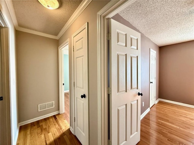 corridor with visible vents, a textured ceiling, baseboards, and wood finished floors