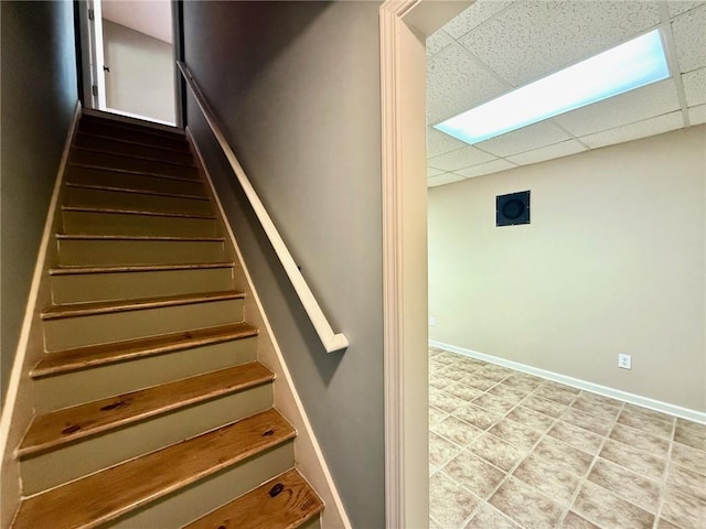 staircase featuring baseboards and a paneled ceiling