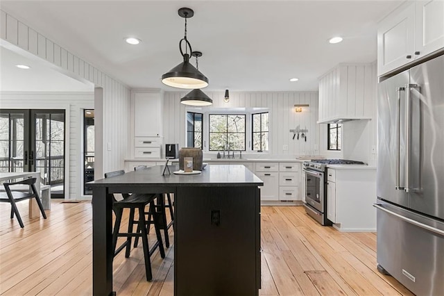 kitchen featuring premium appliances, light wood finished floors, white cabinetry, a sink, and premium range hood