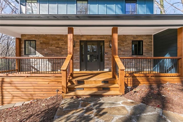 view of exterior entry featuring board and batten siding, covered porch, and stone siding