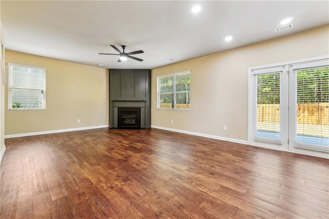 unfurnished living room featuring ceiling fan, dark wood-type flooring, plenty of natural light, and a fireplace