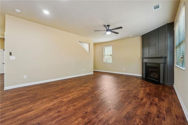 unfurnished living room with dark wood-type flooring, a large fireplace, and ceiling fan