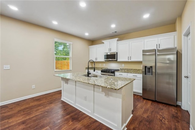 kitchen featuring a center island with sink, sink, light stone countertops, stainless steel appliances, and white cabinets