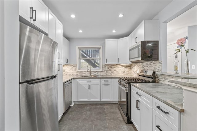 kitchen with light stone counters, stainless steel appliances, decorative backsplash, white cabinets, and a sink