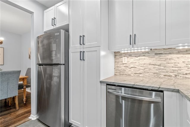 kitchen with white cabinets, light stone counters, wood finished floors, stainless steel appliances, and backsplash