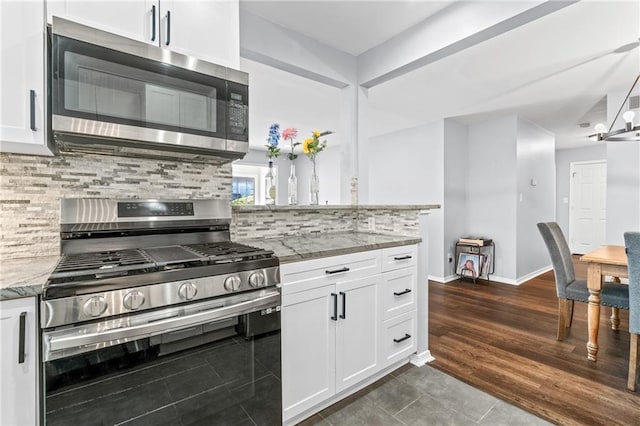 kitchen featuring baseboards, white cabinets, light stone countertops, stainless steel appliances, and backsplash