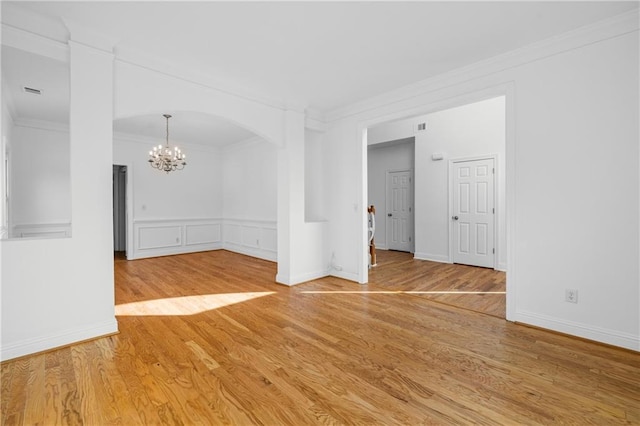 empty room with a wainscoted wall, ornamental molding, wood finished floors, arched walkways, and a notable chandelier