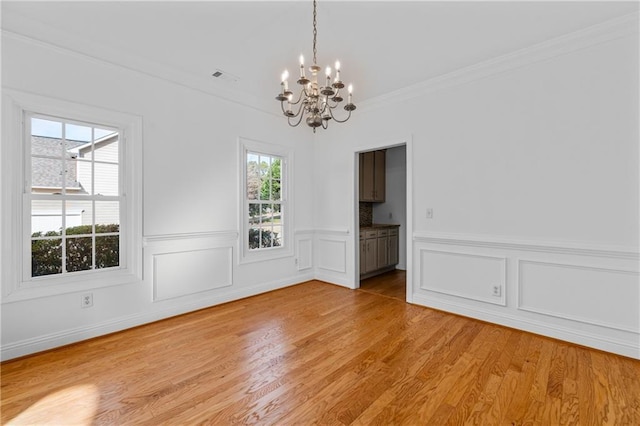 unfurnished dining area with visible vents, light wood-style flooring, wainscoting, crown molding, and a chandelier