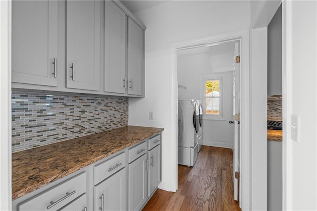 kitchen featuring wood finished floors, baseboards, stone counters, washing machine and dryer, and tasteful backsplash