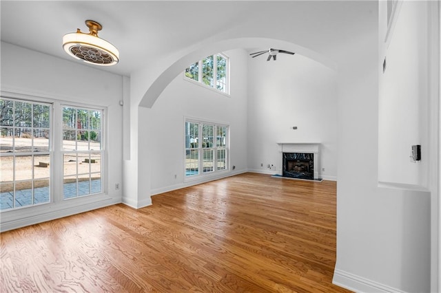 unfurnished living room with a premium fireplace, arched walkways, baseboards, and wood finished floors