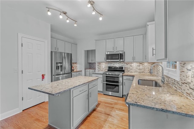 kitchen featuring a center island, gray cabinets, light wood-style flooring, stainless steel appliances, and a sink