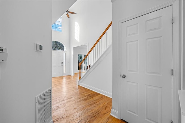 entrance foyer featuring visible vents, a ceiling fan, light wood-style floors, baseboards, and stairs