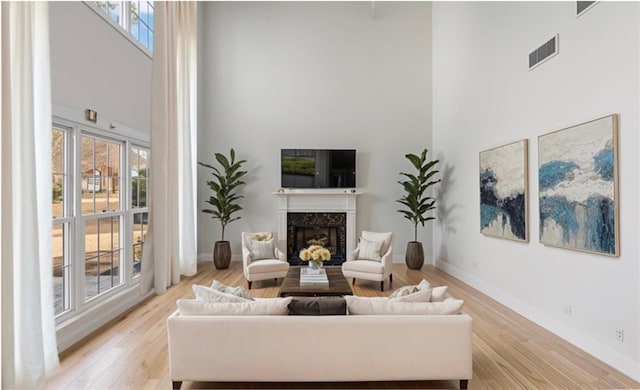 living room with visible vents, light wood-style flooring, a high end fireplace, a high ceiling, and baseboards