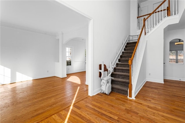 staircase featuring baseboards, arched walkways, a high ceiling, and wood finished floors