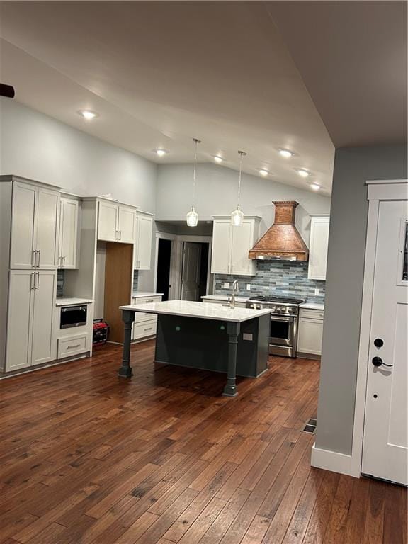 kitchen with a kitchen bar, premium range hood, a center island with sink, decorative light fixtures, and stainless steel range oven