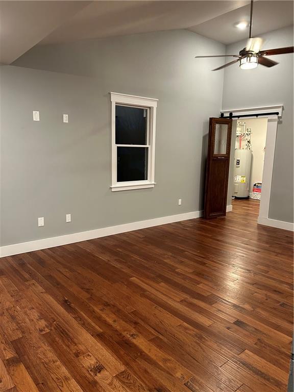 empty room featuring ceiling fan, a barn door, electric water heater, dark hardwood / wood-style flooring, and lofted ceiling