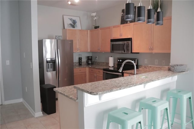 kitchen featuring a breakfast bar area, kitchen peninsula, light brown cabinetry, and stainless steel appliances