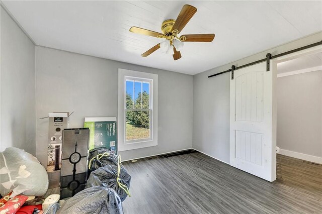 unfurnished bedroom featuring a barn door, ceiling fan, and hardwood / wood-style floors