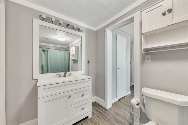 bathroom featuring wood-type flooring, toilet, vanity, and ornamental molding