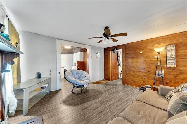 living room featuring hardwood / wood-style flooring, wood walls, and ceiling fan