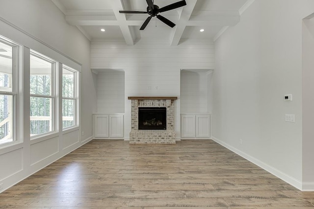 unfurnished living room with a fireplace, beam ceiling, crown molding, coffered ceiling, and light wood-type flooring