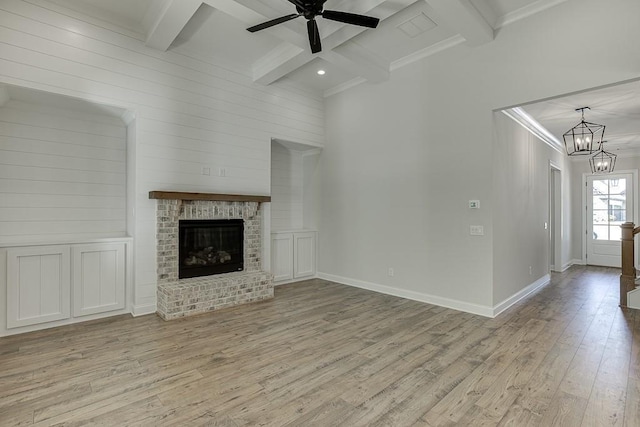 unfurnished living room featuring light hardwood / wood-style floors, a brick fireplace, ceiling fan with notable chandelier, crown molding, and beam ceiling