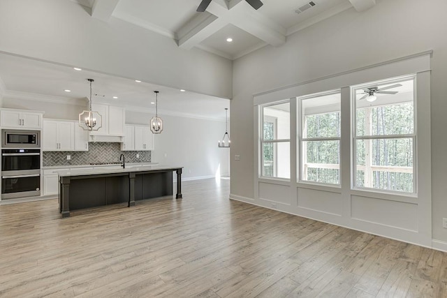 kitchen with coffered ceiling, an island with sink, appliances with stainless steel finishes, pendant lighting, and beam ceiling