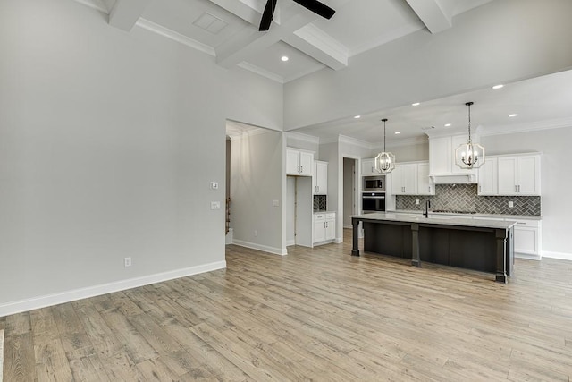 kitchen featuring white cabinetry, coffered ceiling, a kitchen island with sink, pendant lighting, and beamed ceiling