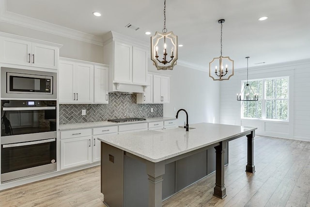 kitchen featuring appliances with stainless steel finishes, white cabinetry, hanging light fixtures, and an island with sink