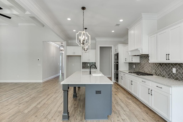 kitchen featuring light stone countertops, an island with sink, white cabinetry, and pendant lighting