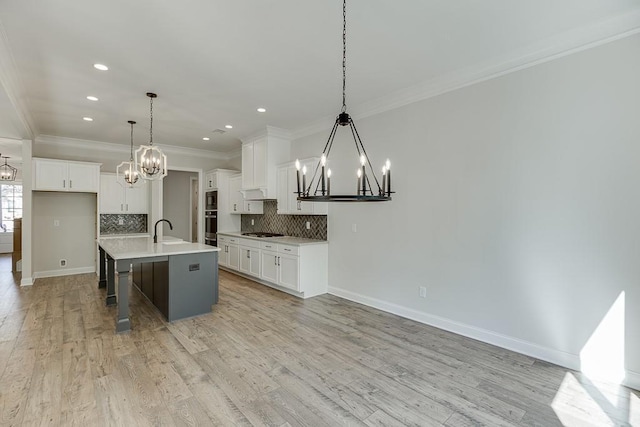 kitchen with hanging light fixtures, white cabinets, a kitchen island with sink, and stainless steel gas cooktop