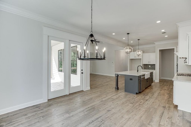 kitchen with tasteful backsplash, a center island with sink, sink, hanging light fixtures, and white cabinets