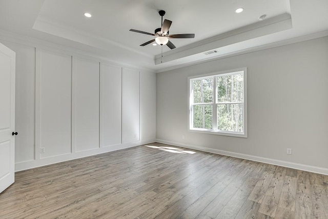 spare room with ceiling fan, ornamental molding, a raised ceiling, and light wood-type flooring