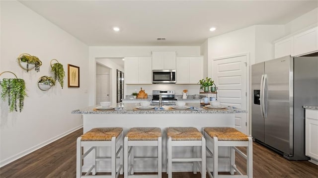 kitchen with white cabinets, a breakfast bar area, stainless steel appliances, and dark wood finished floors