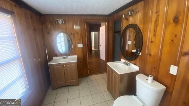 bathroom with toilet, two vanities, a sink, and wood walls