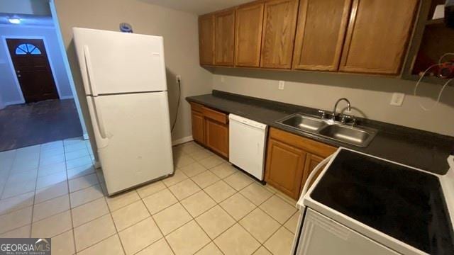 kitchen featuring light tile patterned floors, a sink, dark countertops, white appliances, and brown cabinetry