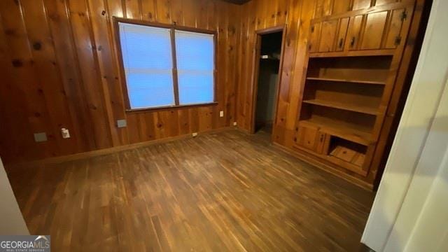 unfurnished living room with wood walls, wood finished floors, and baseboards