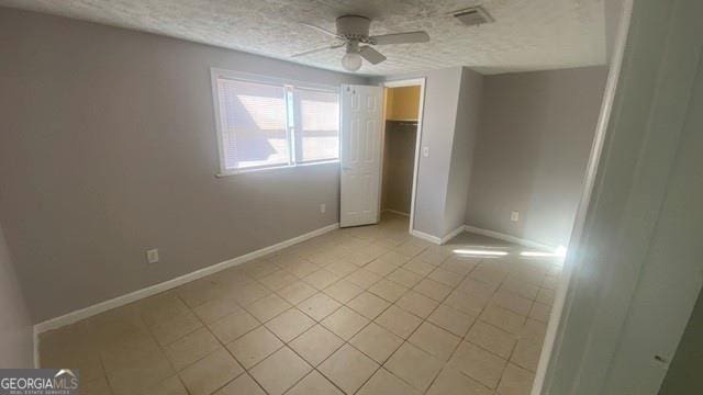 unfurnished bedroom with baseboards, visible vents, a ceiling fan, a textured ceiling, and light tile patterned flooring