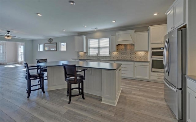 kitchen featuring appliances with stainless steel finishes, custom range hood, a sink, and light wood finished floors