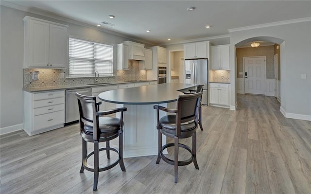 kitchen featuring arched walkways, white cabinets, appliances with stainless steel finishes, a center island, and a sink