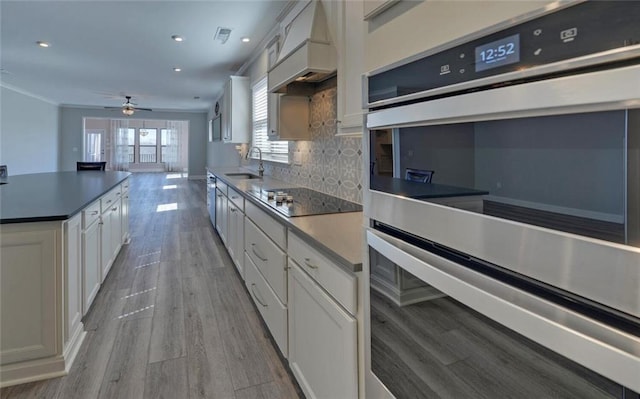 kitchen featuring backsplash, stainless steel double oven, a sink, premium range hood, and black electric cooktop