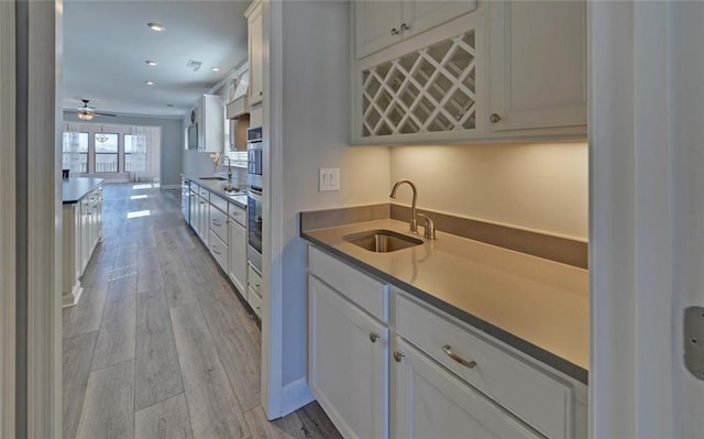 kitchen featuring light wood-style flooring, a sink, stainless steel oven, and white cabinets