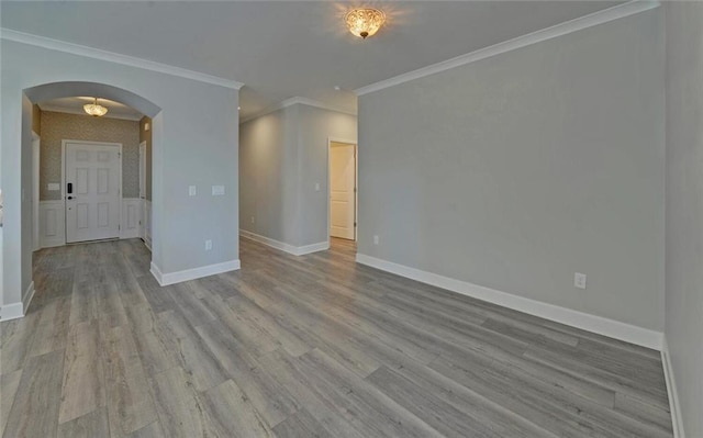 spare room featuring arched walkways, ornamental molding, wood finished floors, and baseboards